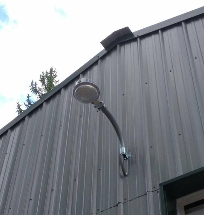 An exterior light on a gooseneck conduit arm on a metal shop wall