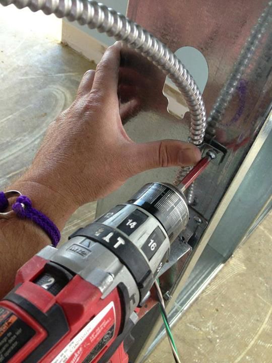 A hand fastening metal-clad cable to a steel stud with a drill