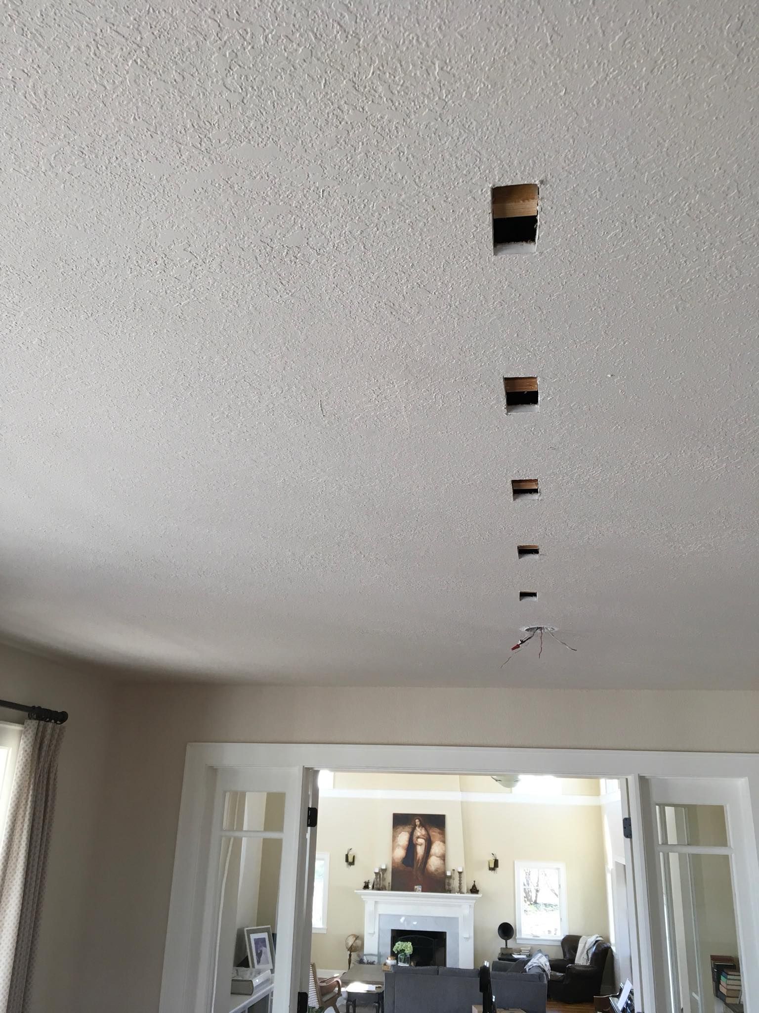 Textured ceiling with a row of small square access holes and loose wires at a fixture box