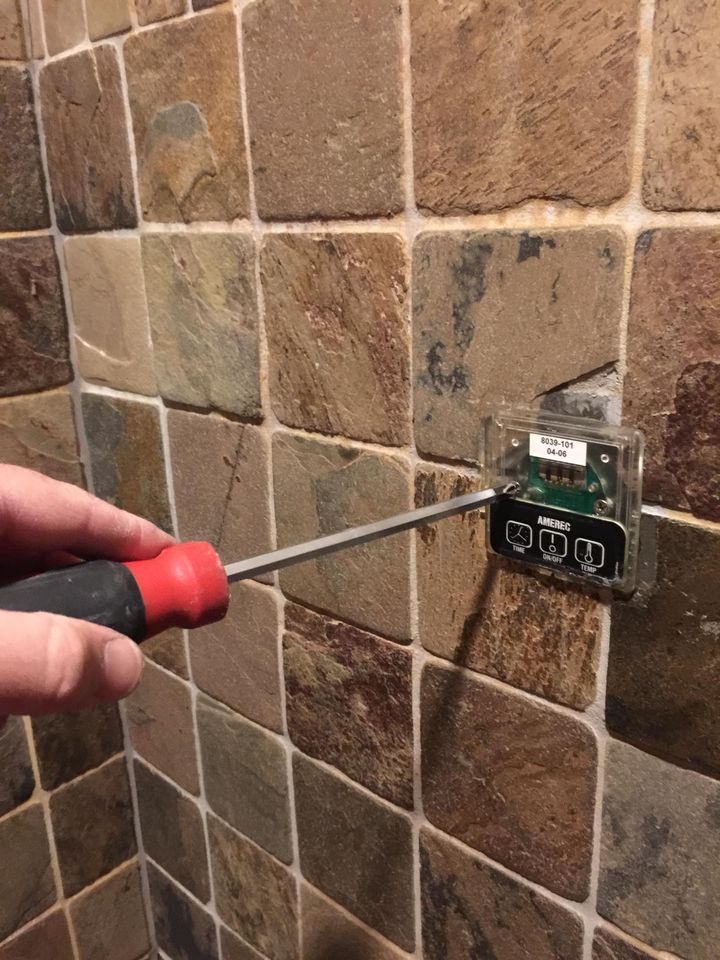 A screwdriver working on a steam shower control set in slate tile