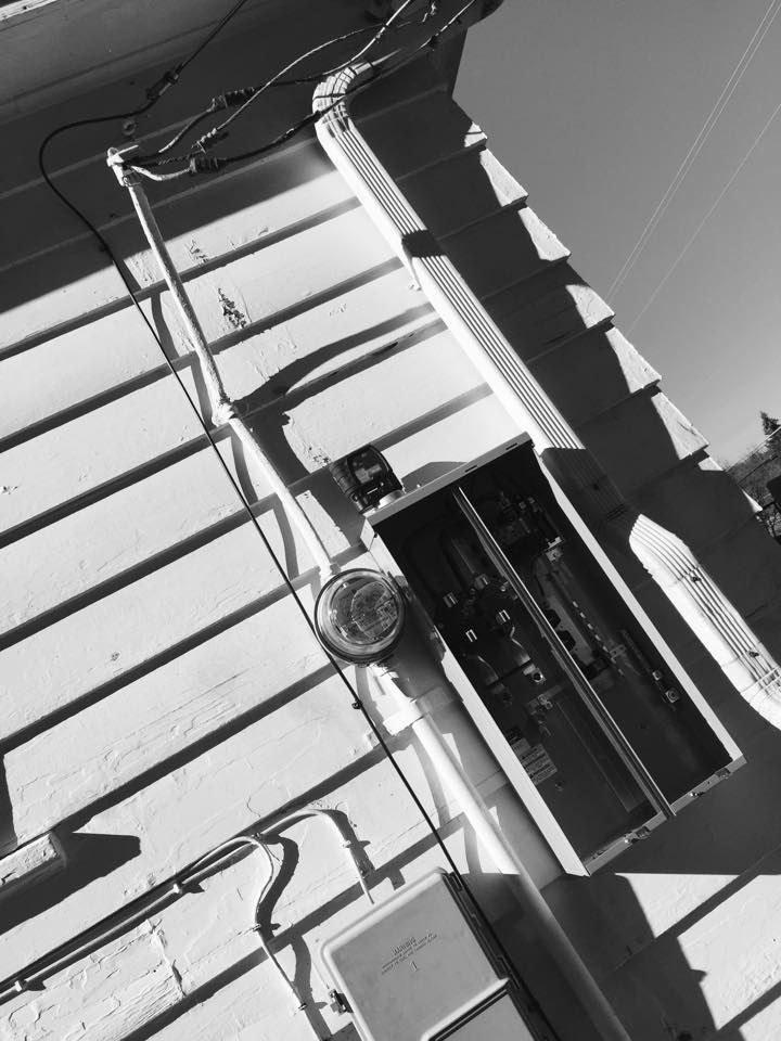 Black and white photo of a meter base and service mast on clapboard siding